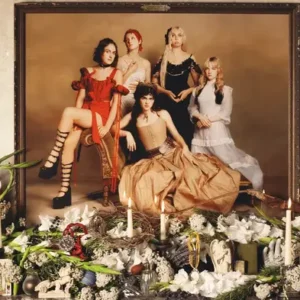 Prelude to Ecstasy by The Last Dinner Party album cover. A photograph of the members of the band The Last Dinner Party in vintage dresses hangs on a mantel covered in candles, greenery, and other miscellaneous objects.