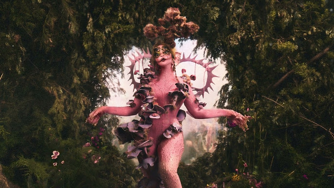 PORTALS by Melanie Martinez album cover. Melanie Martinez in pink alienesque costume surrounded by mushrooms, greenery, and purple flowers that spell out “Portals”