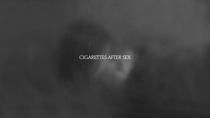 X's by Cigarettes After Sex album cover. The logo for the band Cigarettes After Sex in white font against a blurry black and white background vaguely depicting a man and woman kissing.